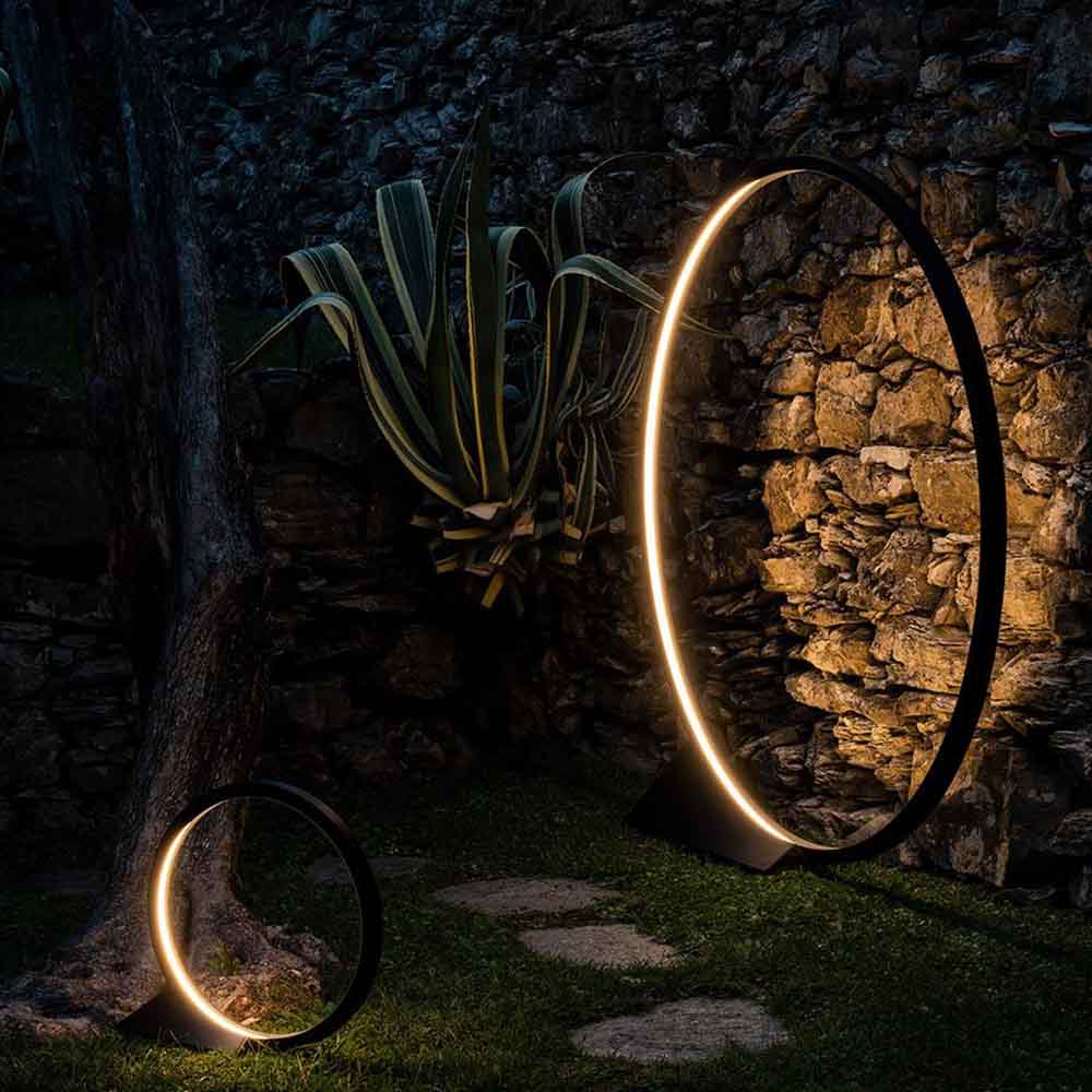 lampada da terra Artemide O che illumina un muro di mattoni in un giardino